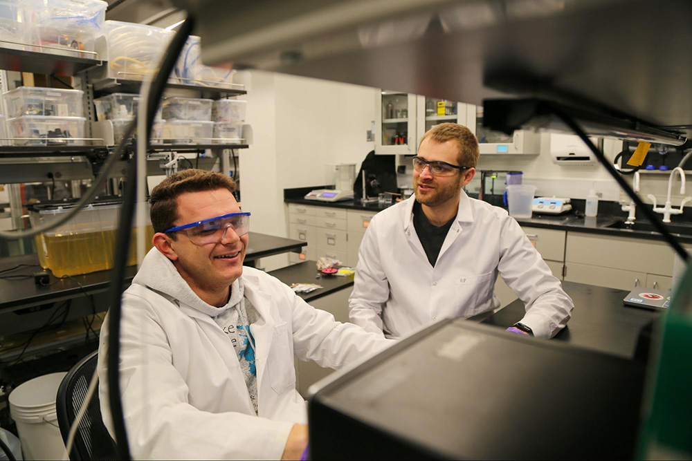 Jack-William Barotta and Dan Harris in teaching lab wearing lab coats and goggles